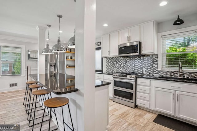 kitchen featuring stainless steel appliances, a sink, a kitchen bar, decorative backsplash, and white cabinetry
