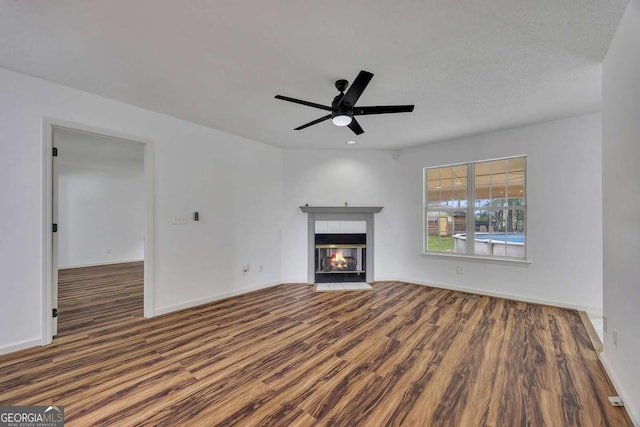 unfurnished living room with wood finished floors, a fireplace, a ceiling fan, and baseboards