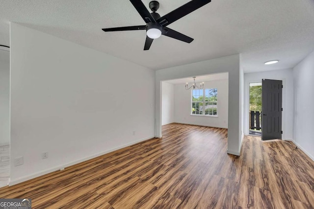 unfurnished living room with a chandelier, wood finished floors, ceiling fan, baseboards, and a textured ceiling