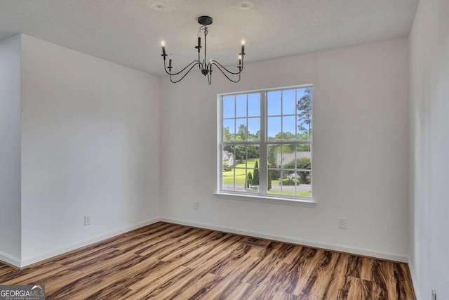 unfurnished dining area with a chandelier, plenty of natural light, wood finished floors, baseboards, and a textured ceiling