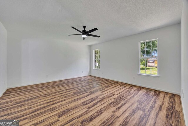 empty room with wood finished floors, baseboards, a ceiling fan, and a textured ceiling