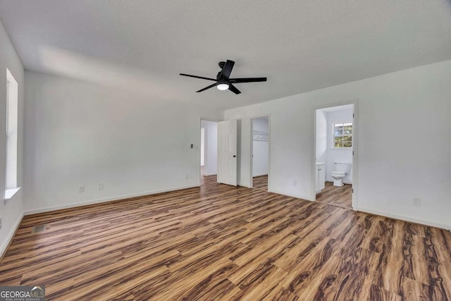 unfurnished bedroom featuring wood finished floors, ensuite bathroom, baseboards, a walk in closet, and a closet