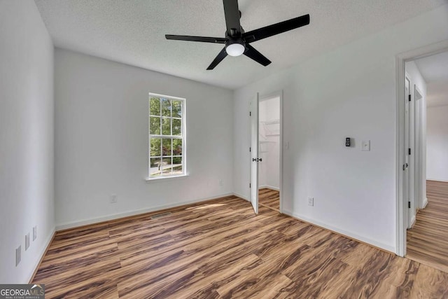 unfurnished bedroom featuring wood finished floors, a textured ceiling, ceiling fan, baseboards, and a spacious closet