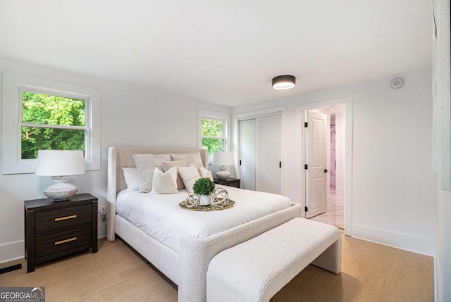 bedroom featuring light wood-type flooring, baseboards, a closet, and ensuite bath