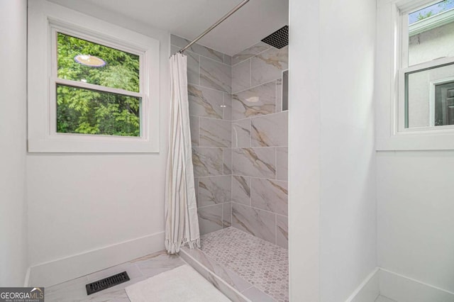 bathroom featuring baseboards, a tile shower, and marble look tile flooring