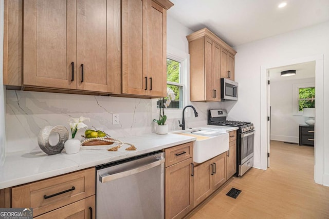 kitchen featuring appliances with stainless steel finishes, a sink, tasteful backsplash, light wood finished floors, and recessed lighting