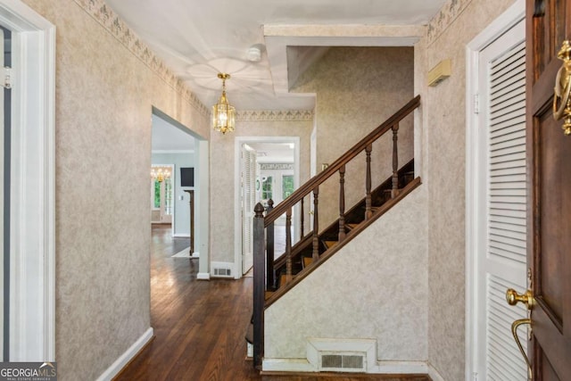 foyer with a chandelier, dark wood-style flooring, stairway, wallpapered walls, and crown molding
