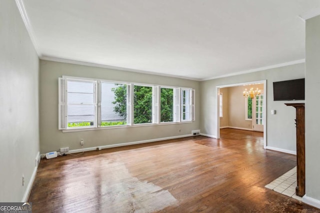 empty room with a chandelier, ornamental molding, wood finished floors, and baseboards