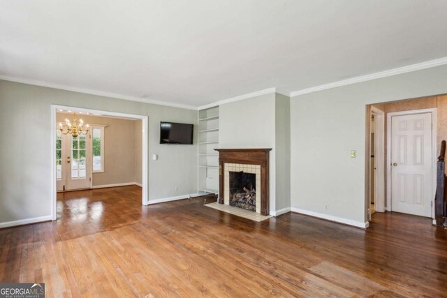 unfurnished living room featuring built in features, a chandelier, wood finished floors, a tiled fireplace, and baseboards