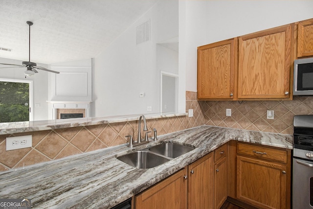 kitchen with appliances with stainless steel finishes, a sink, backsplash, a ceiling fan, and light stone counters