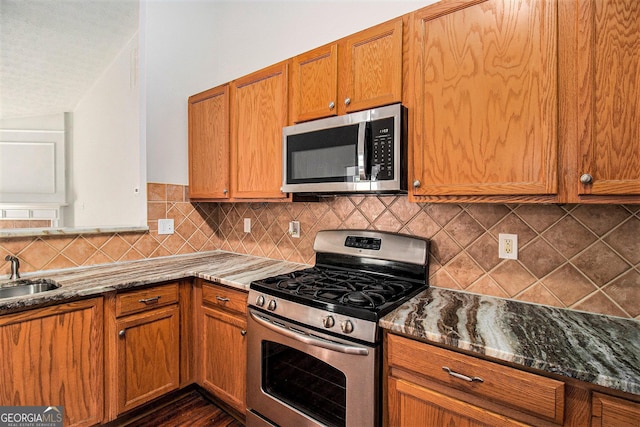 kitchen with appliances with stainless steel finishes, dark stone counters, brown cabinetry, and backsplash