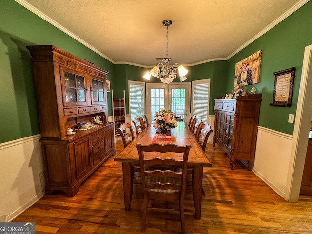 dining space with a chandelier, dark wood finished floors, crown molding, and a wainscoted wall
