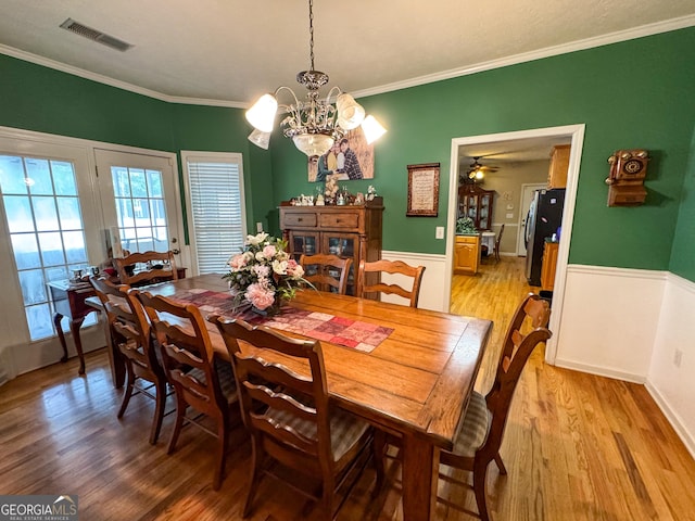 dining room featuring a chandelier, light wood-style flooring, crown molding, and a wainscoted wall