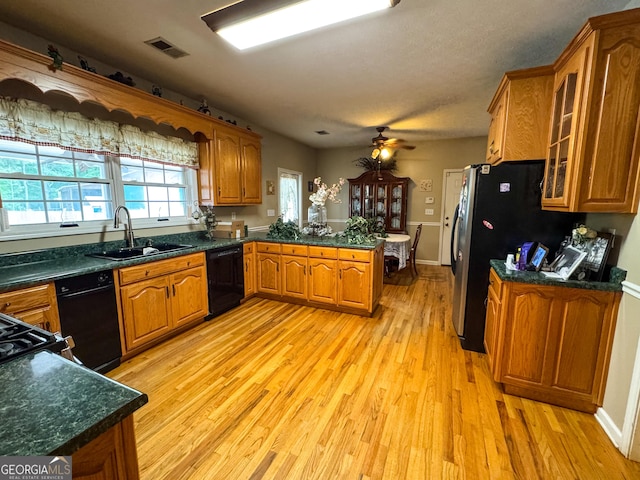 kitchen featuring a peninsula, a sink, brown cabinets, black dishwasher, and light wood finished floors