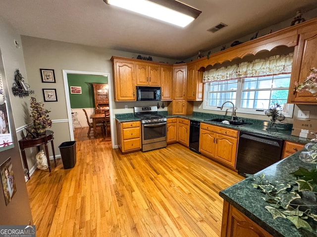 kitchen featuring black appliances, a sink, dark countertops, light wood-type flooring, and brown cabinetry