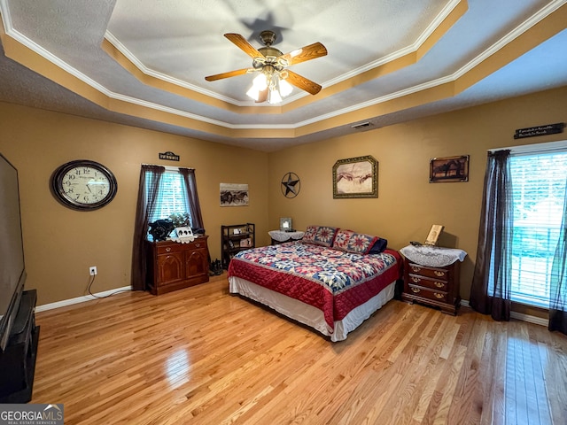 bedroom featuring a raised ceiling, multiple windows, light wood finished floors, ornamental molding, and baseboards
