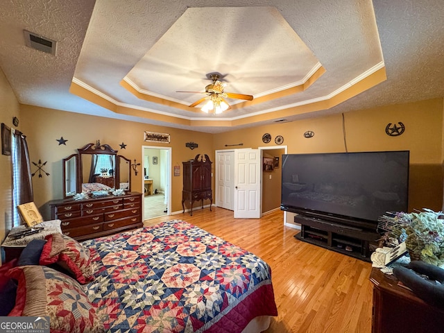 bedroom with a tray ceiling, a textured ceiling, ornamental molding, wood finished floors, and ceiling fan