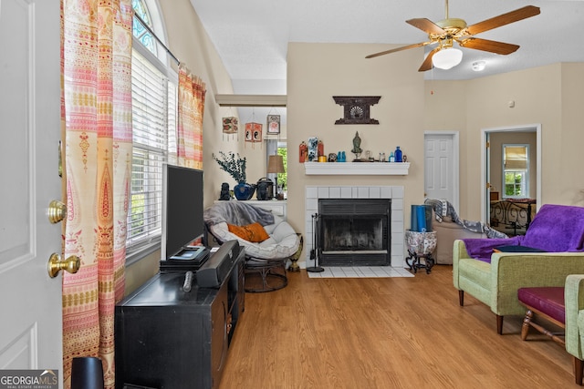 living area with a tiled fireplace, wood finished floors, ceiling fan, and plenty of natural light