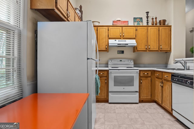 kitchen with white appliances, under cabinet range hood, a sink, brown cabinetry, and light countertops