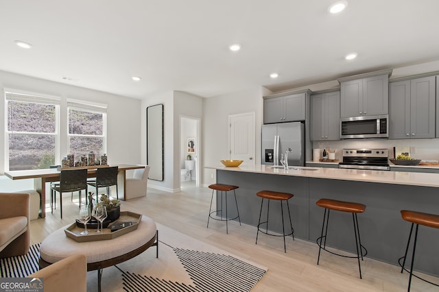 3142 Washburn St, Atlanta, GA 30354 - kitchen featuring appliances with stainless steel finishes, a sink, gray cabinetry, a kitchen bar, and light wood-type flooring