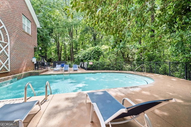 community pool with fence, view of wooded area, and a patio area