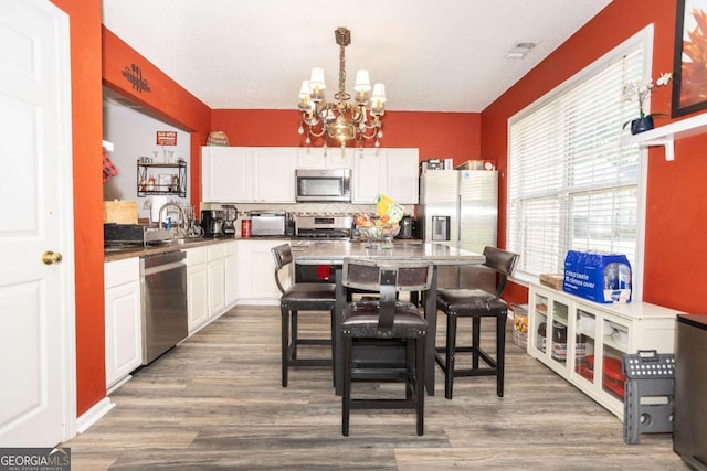 kitchen featuring stainless steel appliances, a chandelier, white cabinetry, decorative backsplash, and wood finished floors
