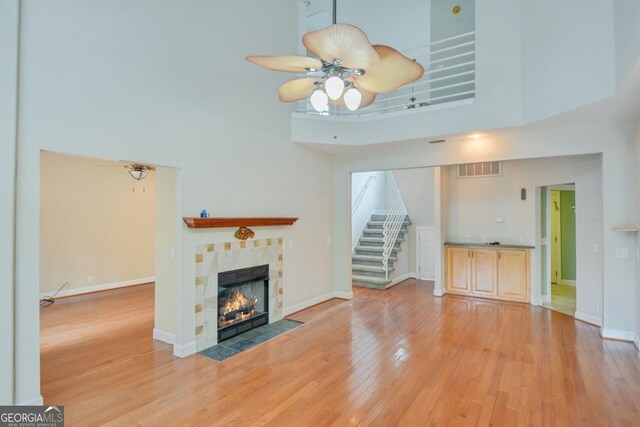 175 Palmera Ln, Brunswick, GA 31525 - unfurnished living room featuring a high ceiling, a tiled fireplace, light wood-style floors, stairs, and a ceiling fan