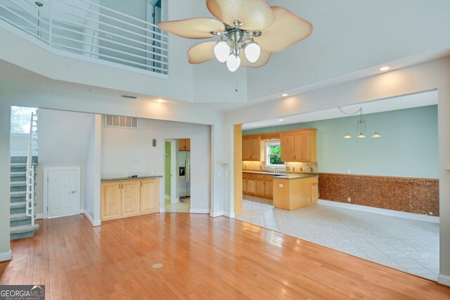 175 Palmera Ln, Brunswick, GA 31525 - unfurnished living room featuring a ceiling fan, light wood-style flooring, a high ceiling, stairs, and baseboards