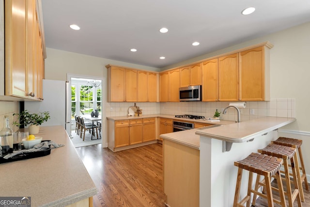 210 Wentworth Ter, Alpharetta, GA 30022 - kitchen featuring appliances with stainless steel finishes, a peninsula, light wood-style floors, light brown cabinets, and recessed lighting