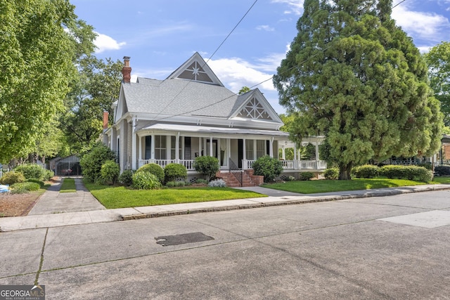 view of front of home featuring covered porch, a chimney, a front lawn, and a shingled roof