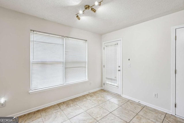 unfurnished room featuring a textured ceiling, baseboards, and light tile patterned floors