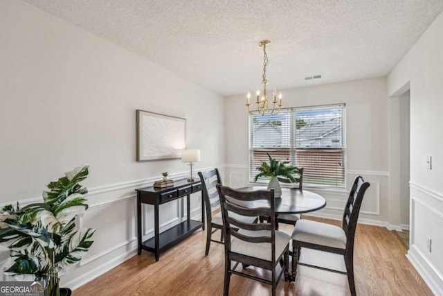 dining space featuring a chandelier, light wood-style floors, a textured ceiling, wainscoting, and a decorative wall