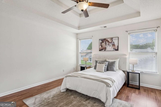 bedroom featuring a raised ceiling, wood finished floors, baseboards, and a ceiling fan