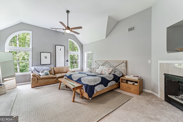 bedroom featuring lofted ceiling, light colored carpet, a tiled fireplace, ceiling fan, and baseboards