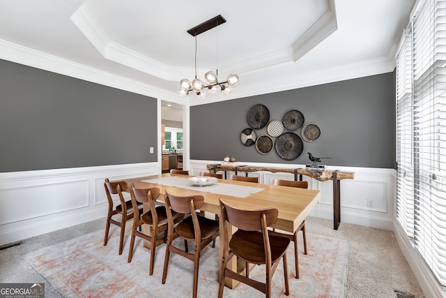 dining area featuring ornamental molding, a wainscoted wall, a raised ceiling, a chandelier, and a decorative wall