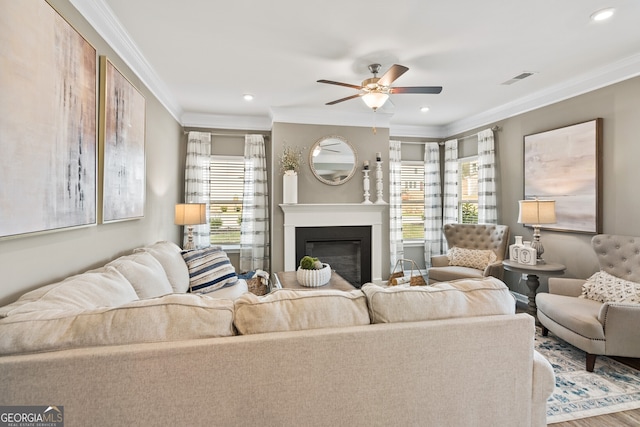 living room featuring healthy amount of natural light, ornamental molding, ceiling fan, a glass covered fireplace, and recessed lighting