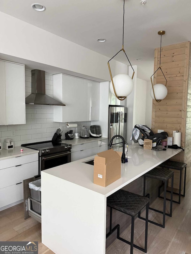 kitchen with wall chimney range hood, modern cabinets, stainless steel appliances, and a kitchen bar