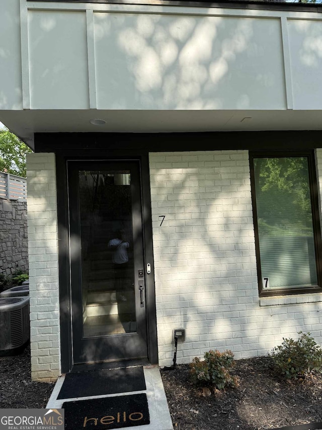 doorway to property featuring brick siding and cooling unit