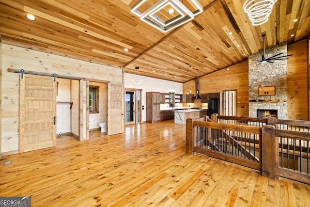 885 Tower Rd, Mineral Bluff, GA 30559 - unfurnished living room featuring light wood-style flooring, wood walls, high vaulted ceiling, a stone fireplace, and a ceiling fan