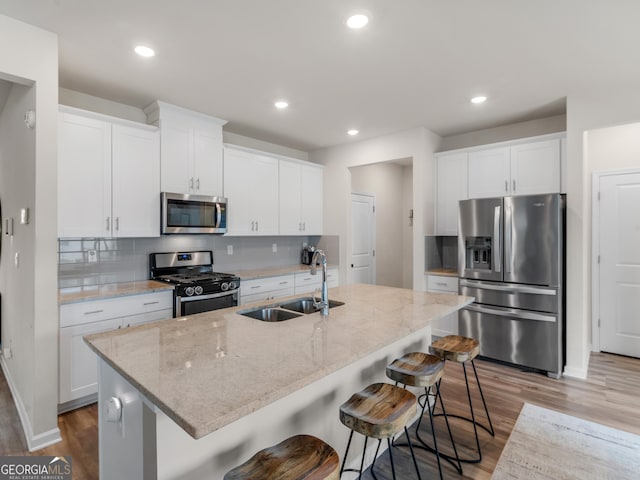kitchen with stainless steel appliances, a sink, light wood-style flooring, tasteful backsplash, and a breakfast bar area