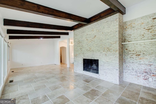 unfurnished living room with arched walkways, stone tile flooring, beamed ceiling, a fireplace, and baseboards