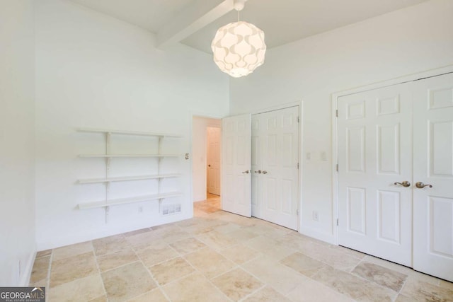 unfurnished bedroom with multiple closets, beam ceiling, light stone finish floors, a chandelier, and baseboards