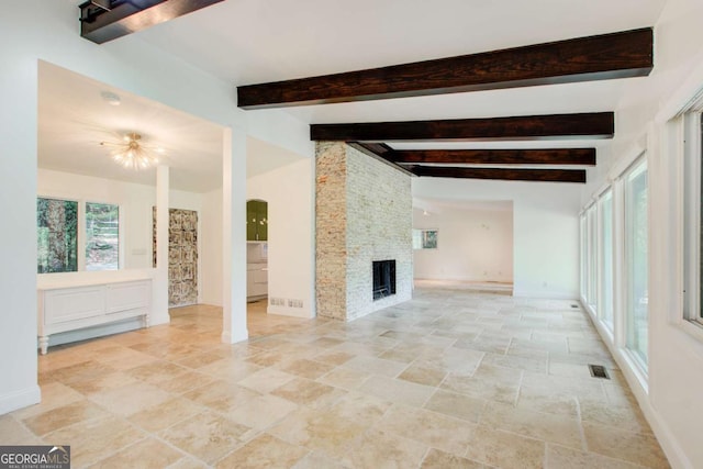 unfurnished living room featuring light stone finish floors, baseboards, beam ceiling, a stone fireplace, and arched walkways