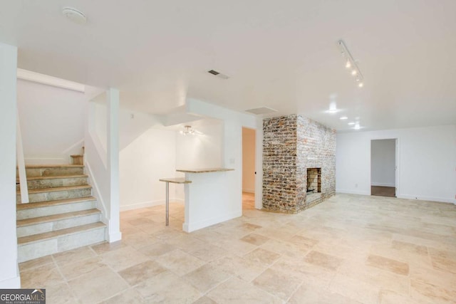 unfurnished living room with stairway, a fireplace, and rail lighting