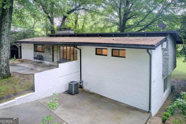 view of property exterior featuring central AC, a patio, and brick siding