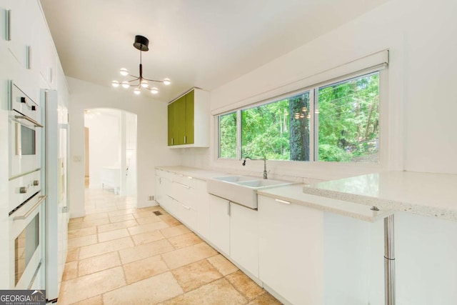 kitchen with a sink, arched walkways, white double oven, and white cabinetry