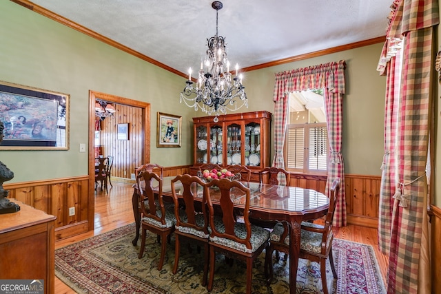 dining room with a wainscoted wall, wood finished floors, wooden walls, a chandelier, and crown molding