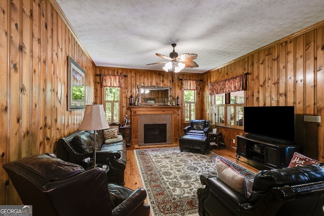 living room with wood walls, wood finished floors, crown molding, a textured ceiling, and ceiling fan