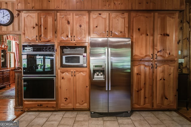 kitchen featuring stainless steel fridge, white microwave, wooden walls, and brown cabinetry
