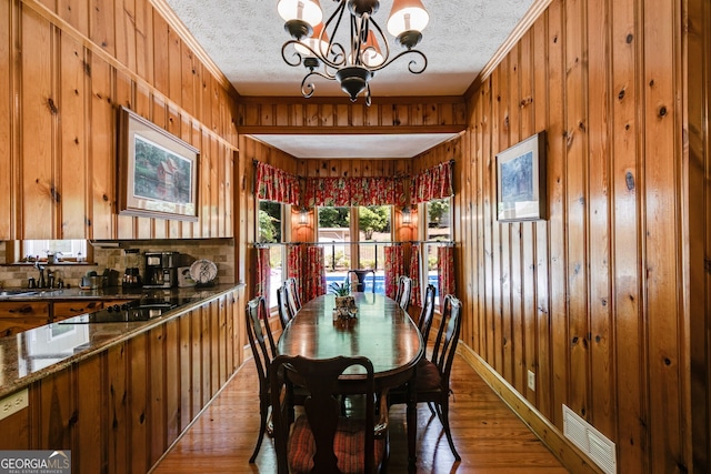 dining space with wood finished floors, a chandelier, wood walls, ornamental molding, and a textured ceiling